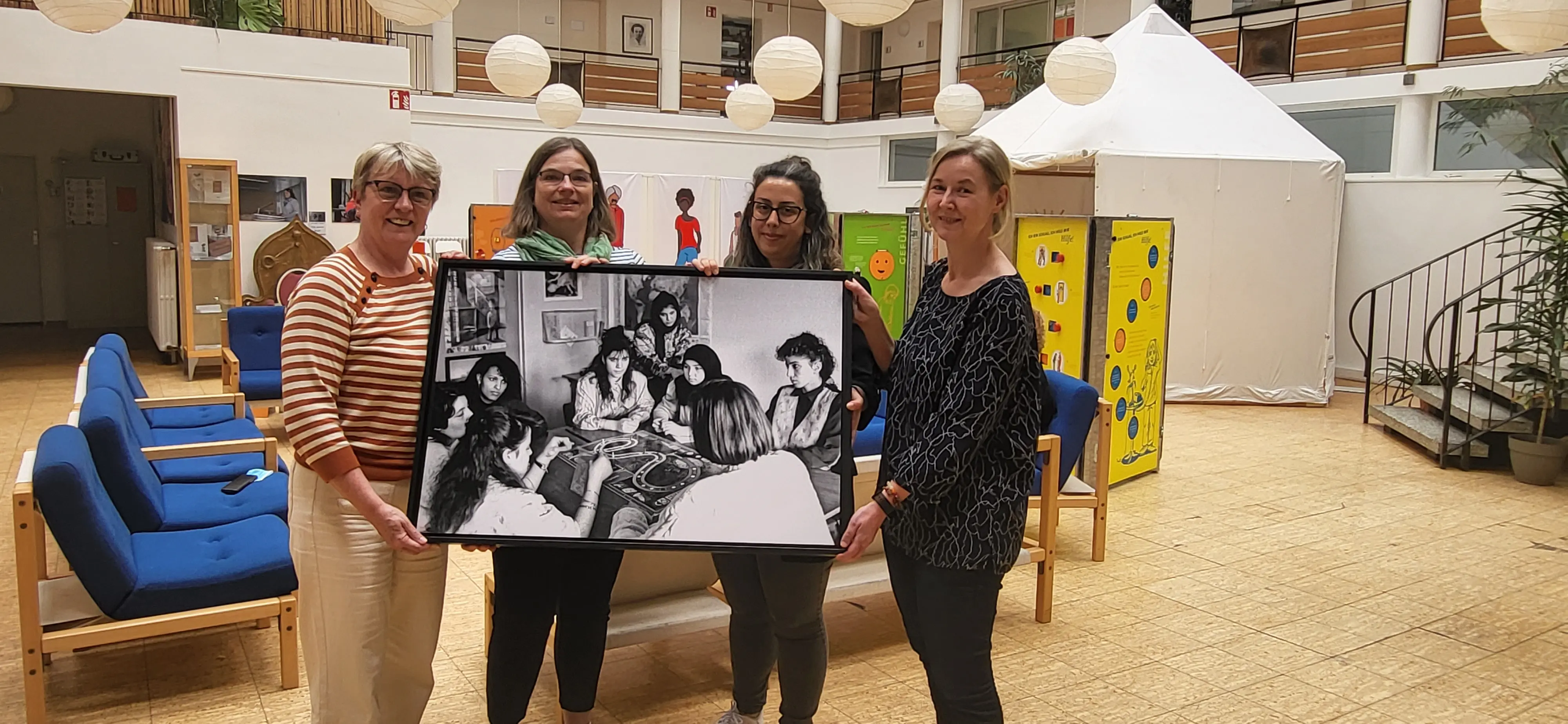 Vier Frauen im Lore Agnes Haus halten ein Bild mit Frauen an einem Tisch, die das Spiel Spielen, hoch