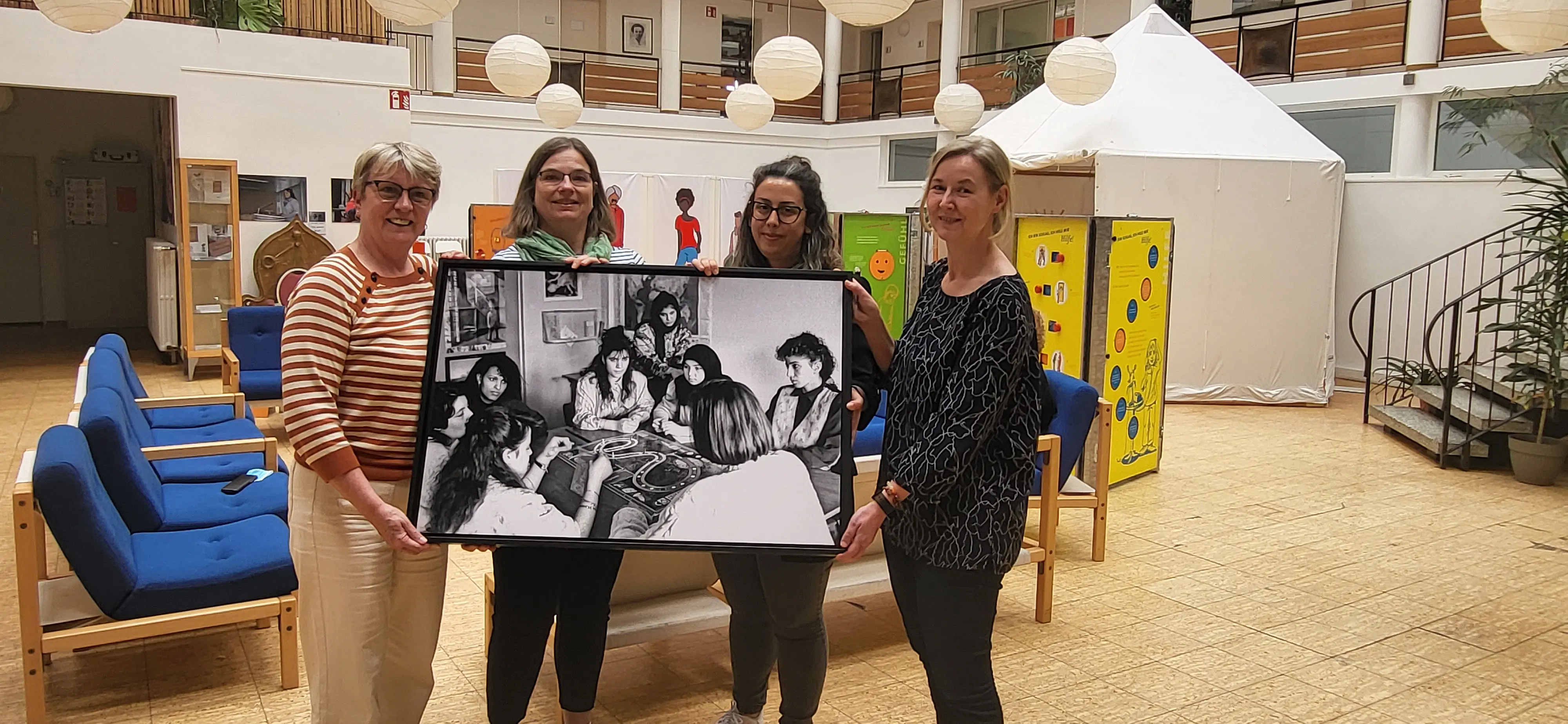 Vier Frauen im Lore Agnes Haus halten ein Bild mit Frauen an einem Tisch, die das Spiel Spielen, hoch